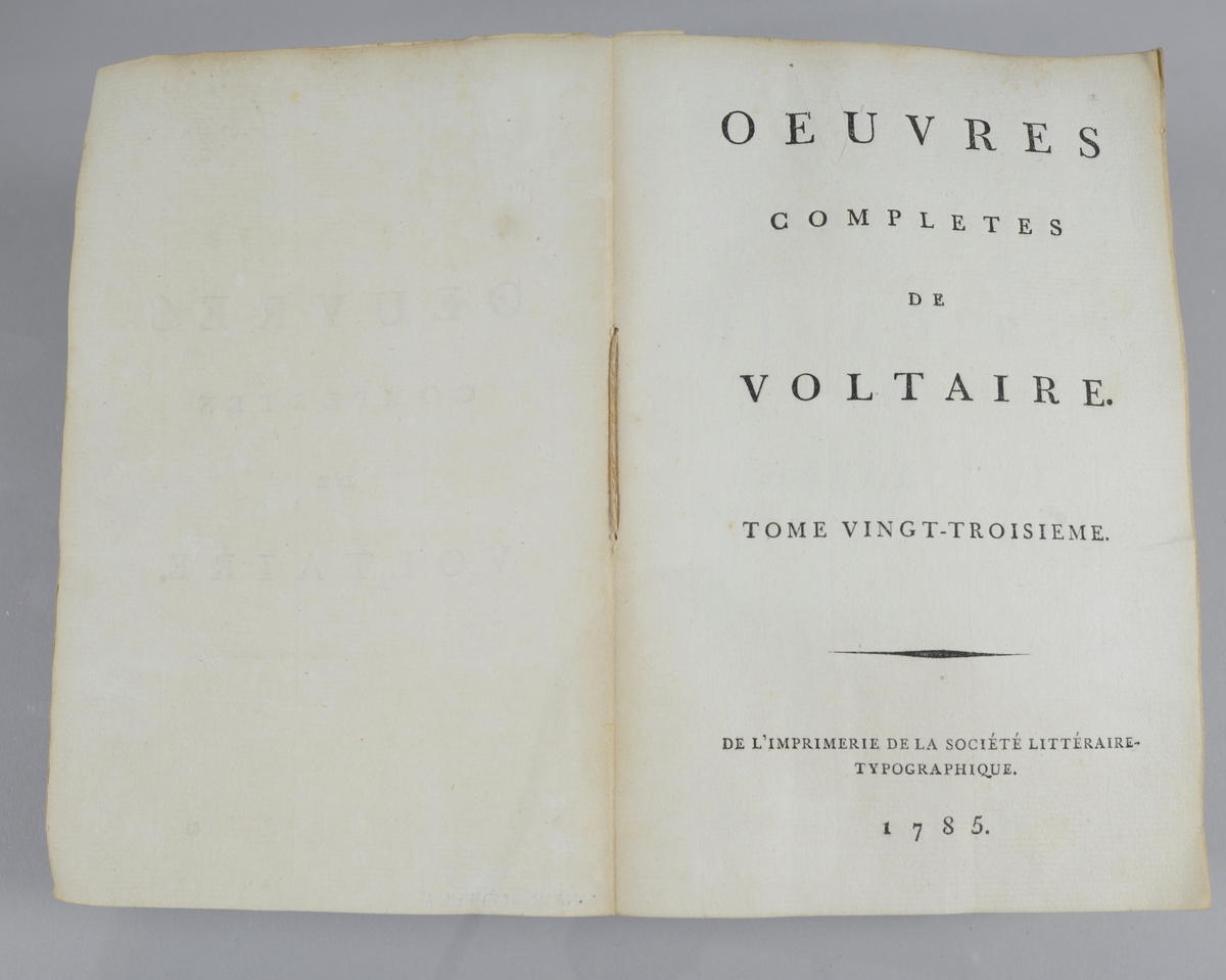 Bok, pappband,"Oeuvres completes de Voltaire", del 23 Histoire de Charles XII, tryckt 1785.
Pärmen klädd med gråblått papper, på pärmens baksida klistrad sida ur annan bok. Med skurna snitt. På ryggen klistrad pappersetikett med tryckt text samt volymens nummer. Ryggen blekt.