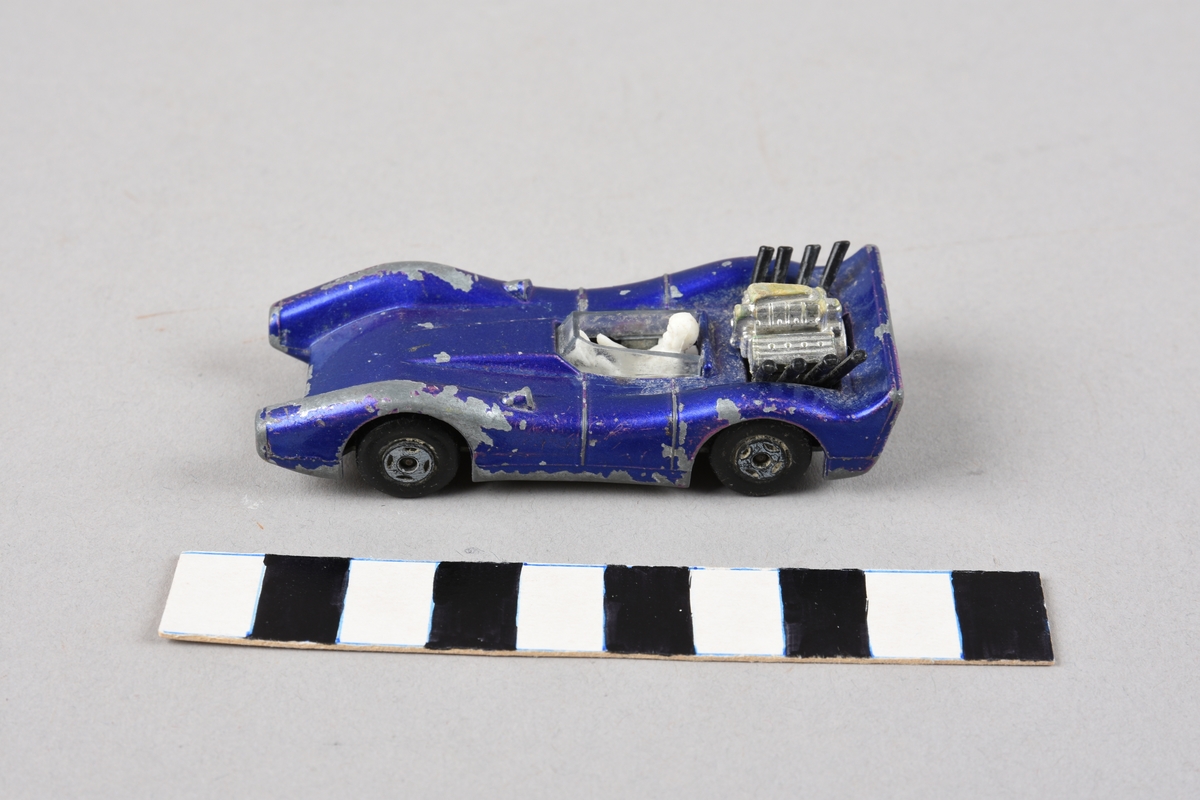 Leikebil, racerbil med høg spoilar bak, synleg del av motor bak førar, som sit bak ei plastskjerm