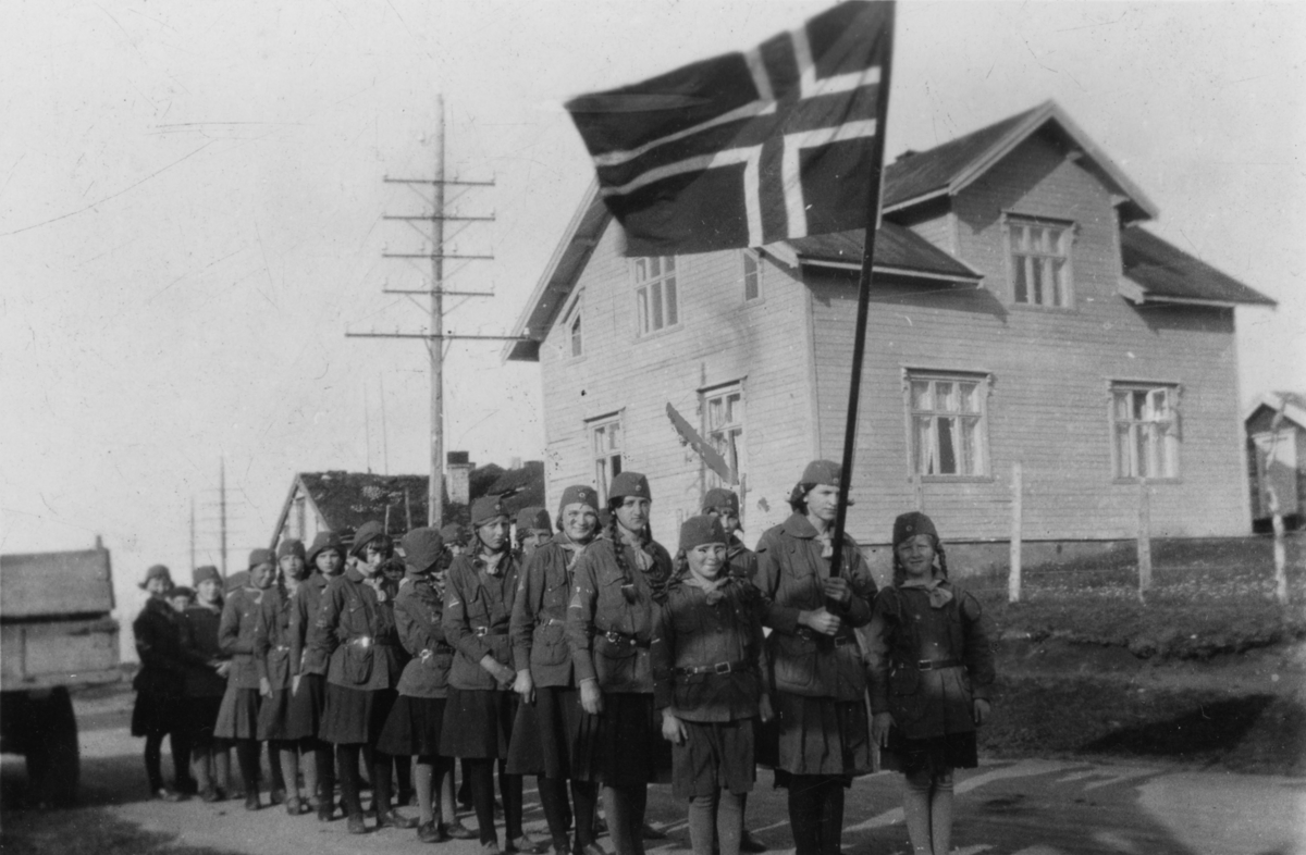 Speiderer på sommerleir i Smalfjord i 1931. Vadsø- og Tanaspeiderne er på vei til kirken på Langnes. Jentene går i tog forbi "Klokkergården", Gjertrud Evanger fra Vadsø bærer flaggen.