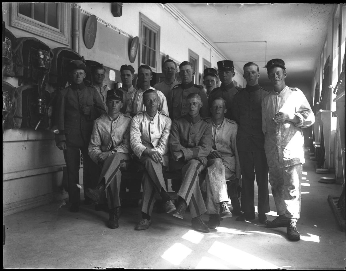 Gruppbild tagen under fotografen Harald Olssons excercistid. På bilden är 14 män uppställda eller sittande i en korridor och klädda i olika typer av uniformer.