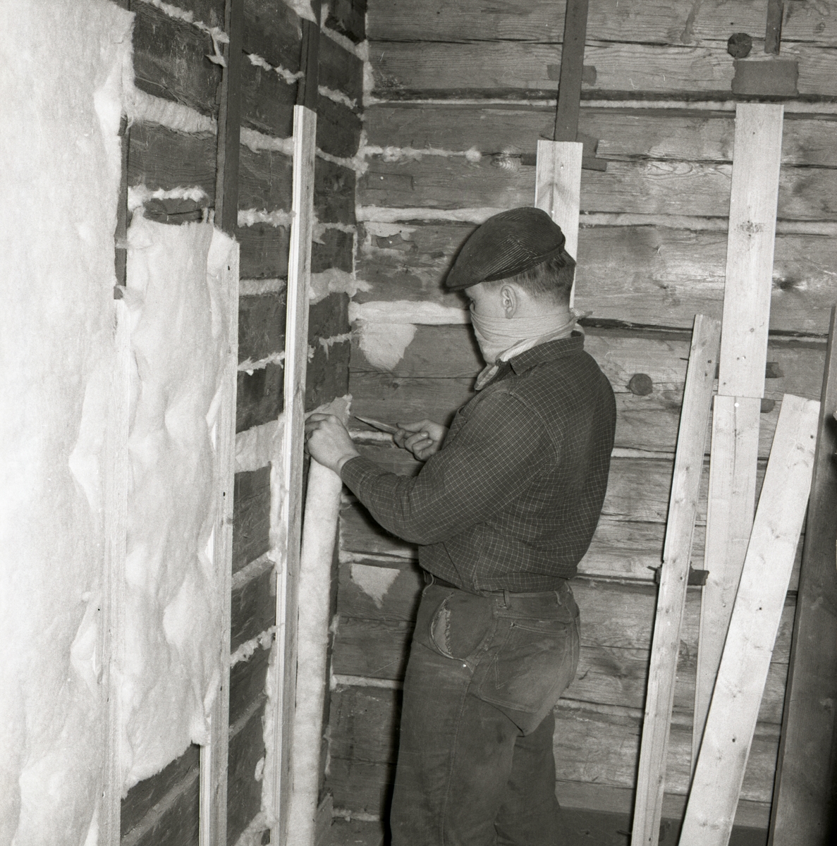 En man isolerar timmerväggar i ett hus på gården Sunnanåker, 1967.