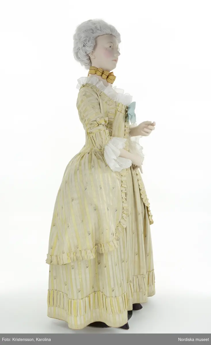 Adelsdam 1780, från utställningen Modemakt. Modellen är fotograferad för 360-visning. Information om kläderna se Relaterade objekt under Referenser. Rynkad volang till halsringning och en övre kant på bröstlappen är rekvisita.