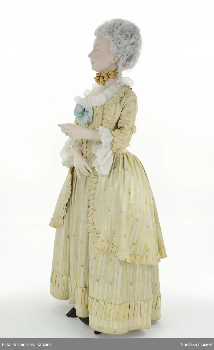 Adelsdam 1780, från utställningen Modemakt. Modellen är fotograferad för 360-visning. Information om kläderna se Relaterade objekt under Referenser. Rynkad volang till halsringning och en övre kant på bröstlappen är rekvisita.