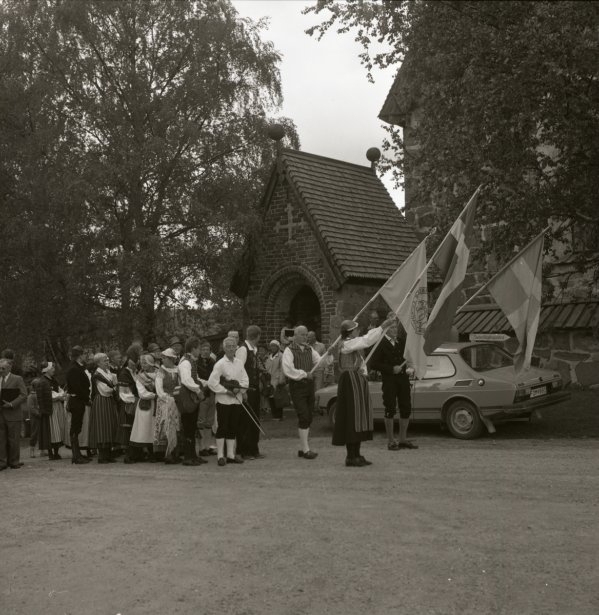Parad med folkdräktsklädda människor framför kyrkan. Först går fanbärare och musikanter , Trönö 16 juni 1985.