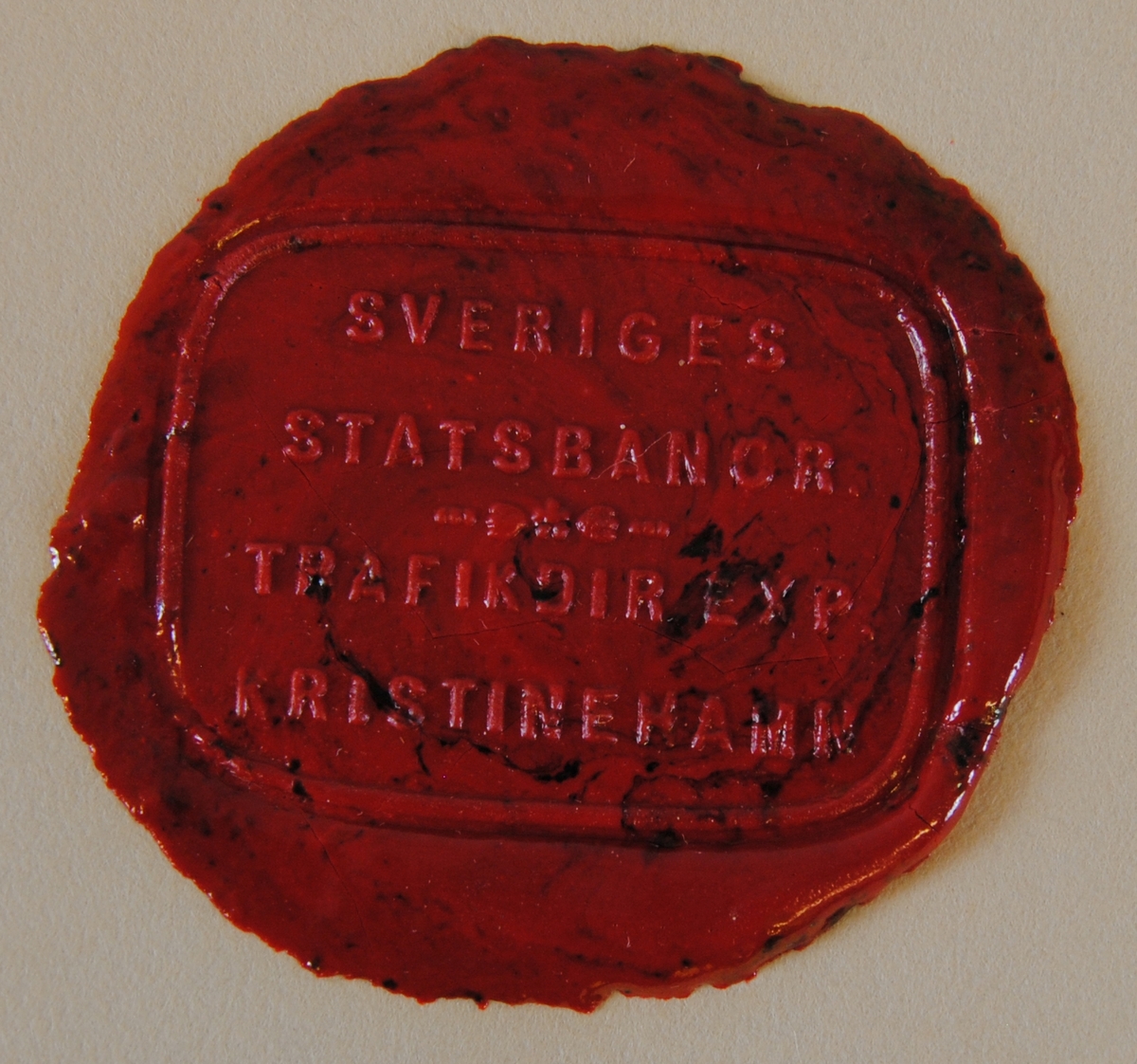 Rektangulärt sigillavtryck med rundade hörn i rött lack på gultonat papper. Texten löper över fyra rader och i mitten finns ett litet blomsterornament.