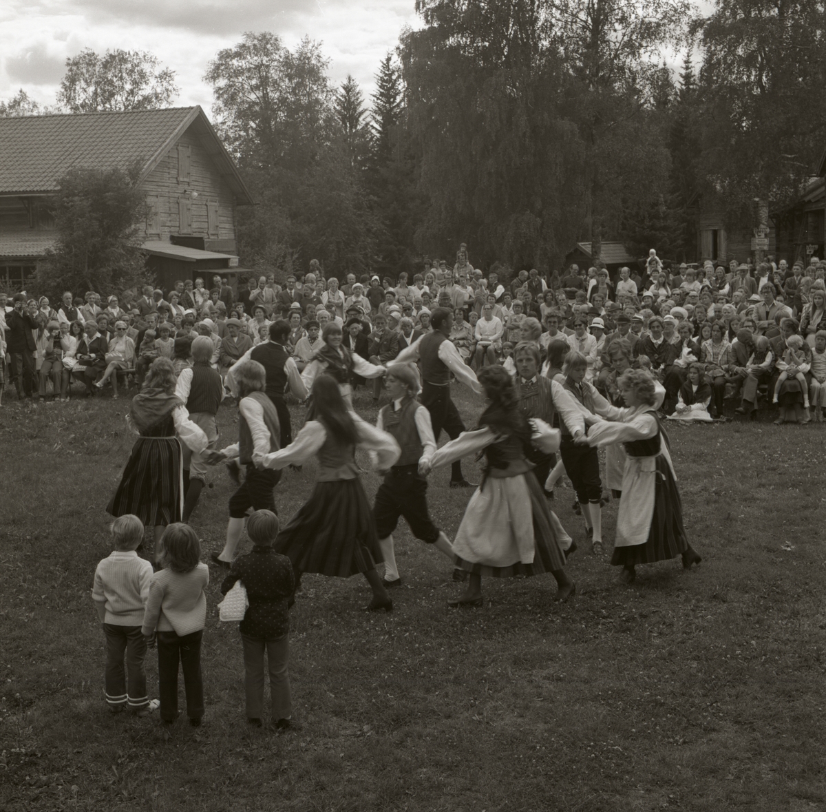 Under Rengsjöfesten vid hembygdsgården betraktar publiken en ringdans. Tre barn tittar nyfiket på dansparen, 1972.
