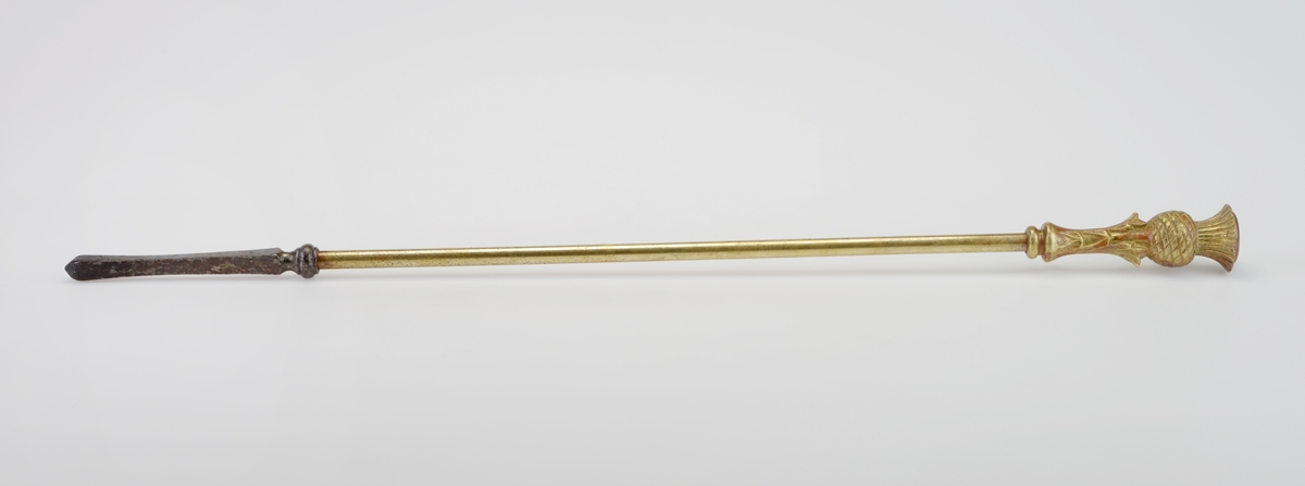 Et peissett/ovnssett bestående av ildrake og peisklype laget av messing som har vært forgylt. Ildraken (FTT.56083.01) består av en messingstang (41cm lang) med et messinghåndtak på toppen. Håndtaket er utformet som en ananasbusk. Nederst på stangen er det festet en 15cm lang spyd laget av jern. Peisklypen (FTT.56083.02) består av to armer som er festet med en skrue øverst. Oppe på armene er det dekor i form av trekløverblader og en rose der de er skrudd sammen. Nederst på klypen er det trekløverblader som fungerer som "hender". Håndtaket er som på ildraken utformet som en ananasbusk.