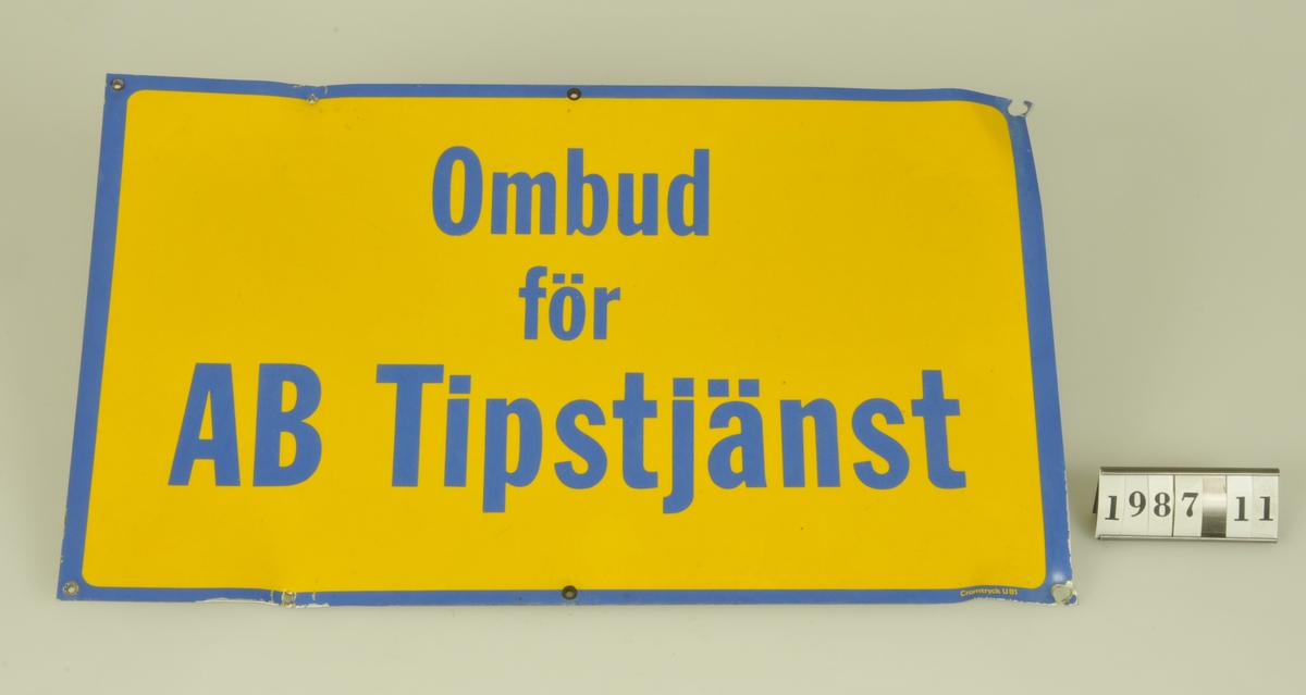 Text: "OMBUD  FÖR AB TIPSTJÄNST". Blå text och kant
mot gul botten.

Kommer från livsmedelsaffären Oskar Nilssons Eftr.
Lärkvägen 15, Alingsås. Affären etablerades 1906
och lades ned i juni 1986.
