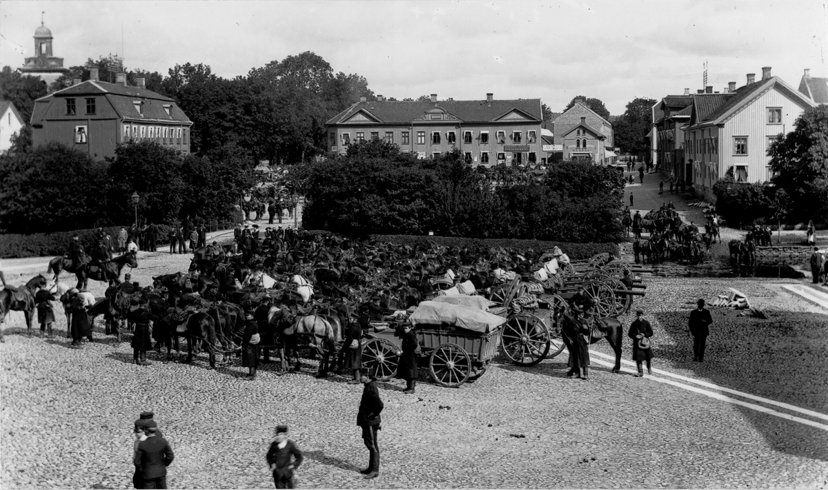 Kungliga Första Göta artilleriregemente rastar på Lilla Torget på marsch till Tåga hed, sommaren 1900. I bakgrunden syns Stora torget.