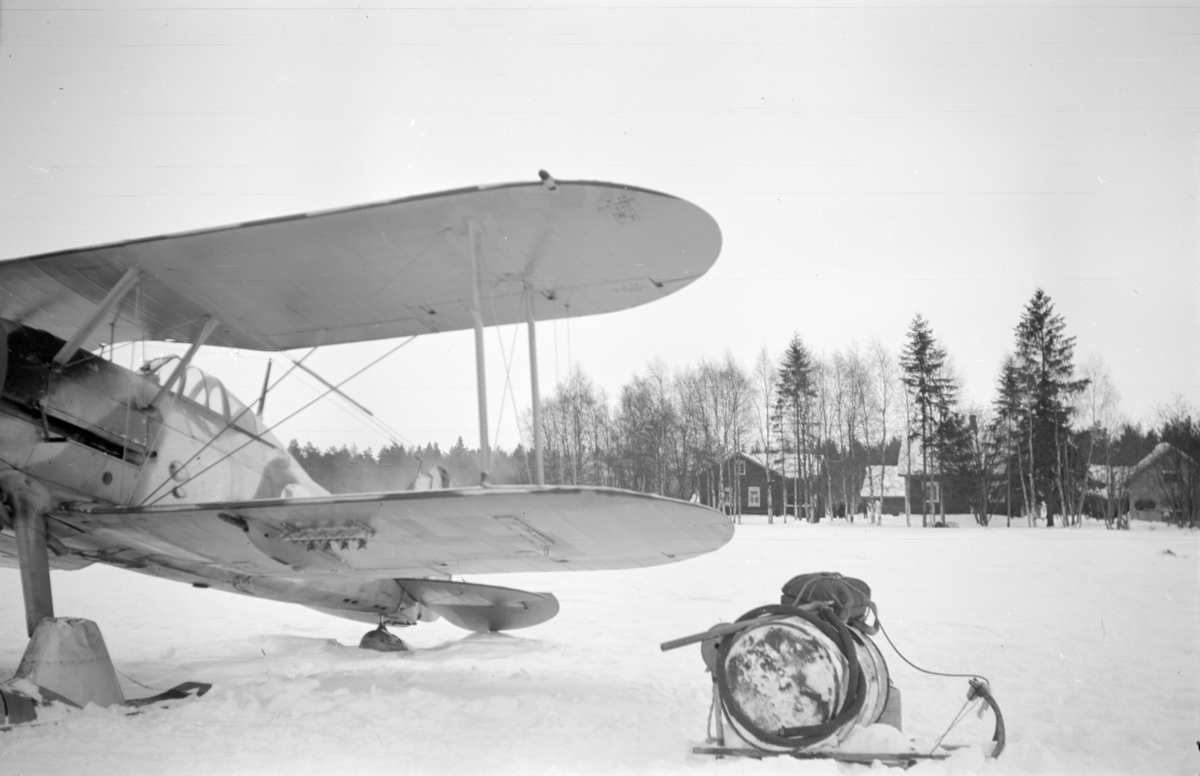 Flygplan Gloster Gladiator märkt gul F uppställd på en flygbas vid F 19, Svenska frivilligkåren i Finland. Till höger syns bensintank och fallskärm.