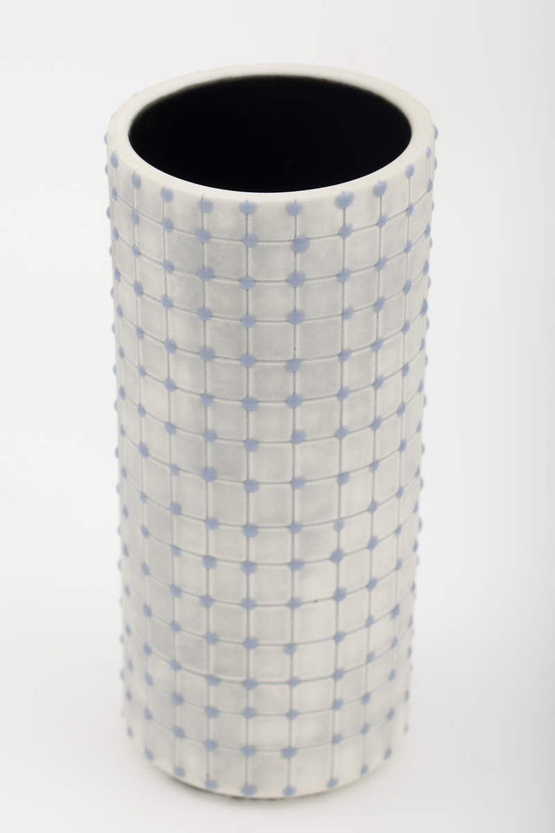 Mellomstor, smal sylinderformet beholder. Gråskimret farge dekorert med gråblått rutenett hvor krysningspunktene er markert med glasuren. Sort innside.