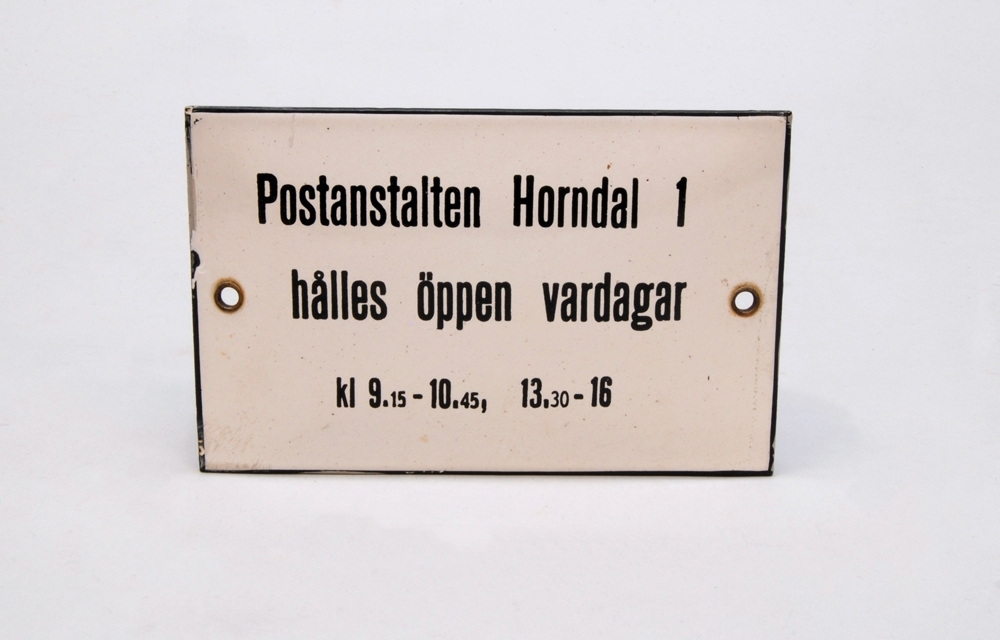 Rektangulär poststationsskylt av emalj. Den har vit botten och svarta kanter. På skylten finns texten: "Postanstalt Horndal 1 hålles öppen vardagar kl 9.15-10.45, 13.30-16", tryckt i svart. Det finns ett hål med öljett på varje kortsida. 

Historik: Givarens far arbetade som stins i Horndal mellan 1952 och 1969. Han var ansvarig för posten som låg i samma rum som hans expeditionsrum. När stationshuset revs någon gång kring 1970 tog givarens mor ned några av skyltarna i byggnaden, bland annat denna som beskriver postens öppettider.