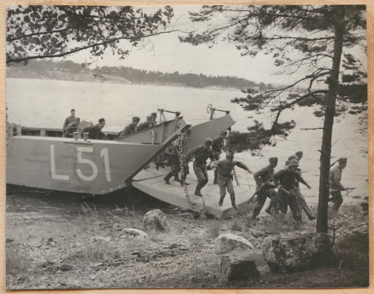 Landstigningsbåten L 51 har lagt till stranden i skärgården under en övning. Rampen har fällts när och soldaterna springer ut från båten.