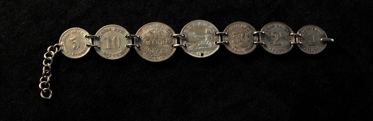 Beskrivning: Ett st. armband, bestående av sju st. tyska och spanska mynt från 1870-talet. På det spanska myntets baksida är ingraverat: "Minne af G & H".