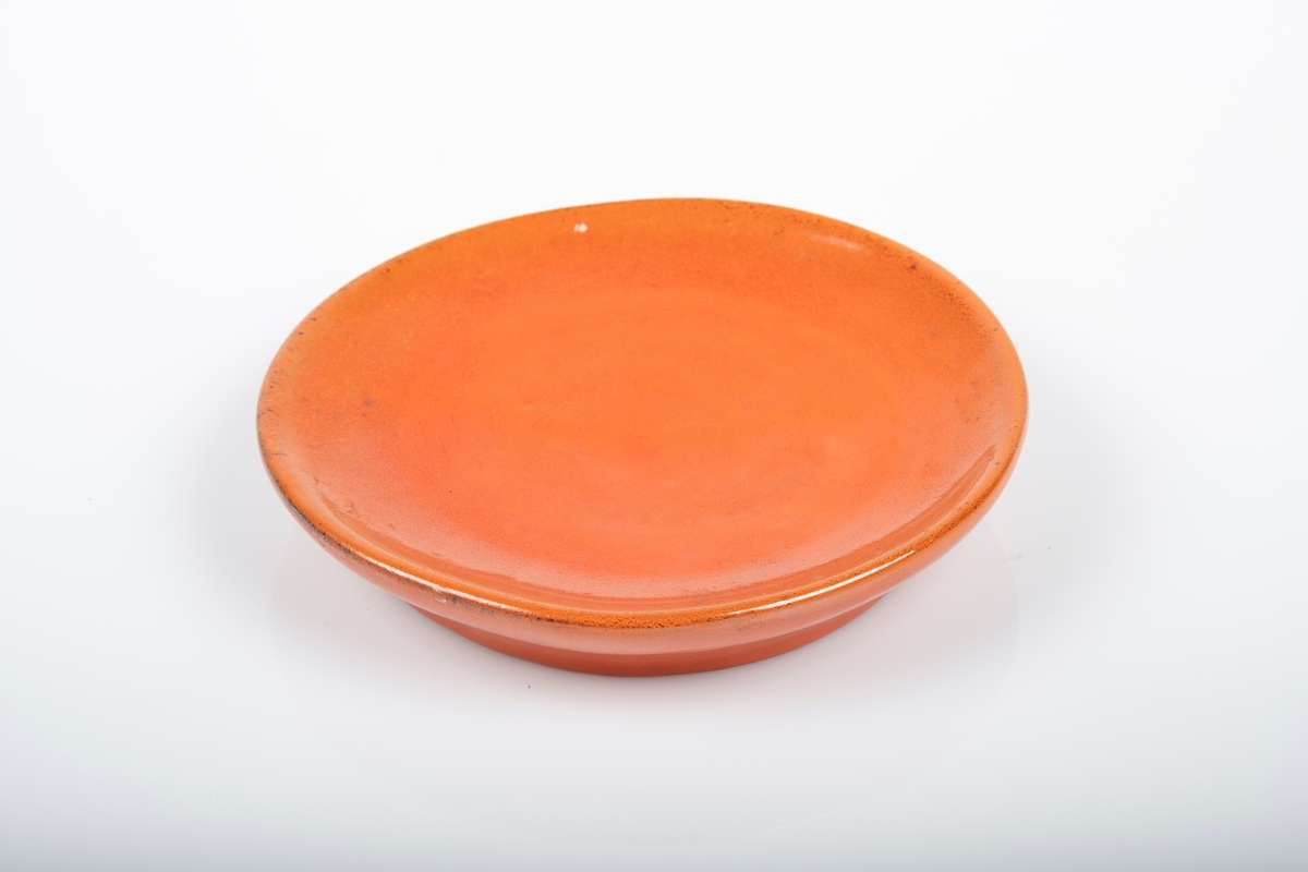 Liten keramikkskål med rød glasur. Det er innskrift på undersiden av skålen.