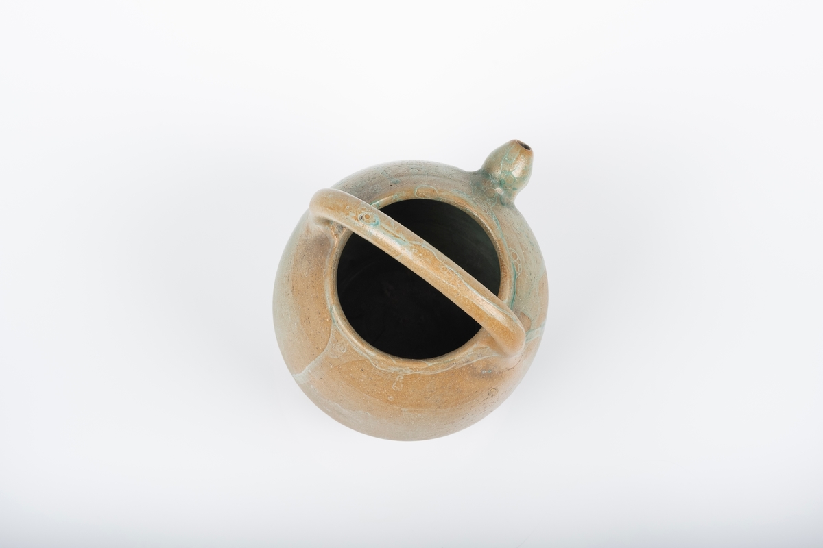 Keramikkanne trolig brukt som tekanne eller vannkanne. Den mangler/har ikke lokk. Den er dreid og har rund form med hank over åpningen. Liten høyt plassert tut. Den er delvis glasert med grønn glasur.