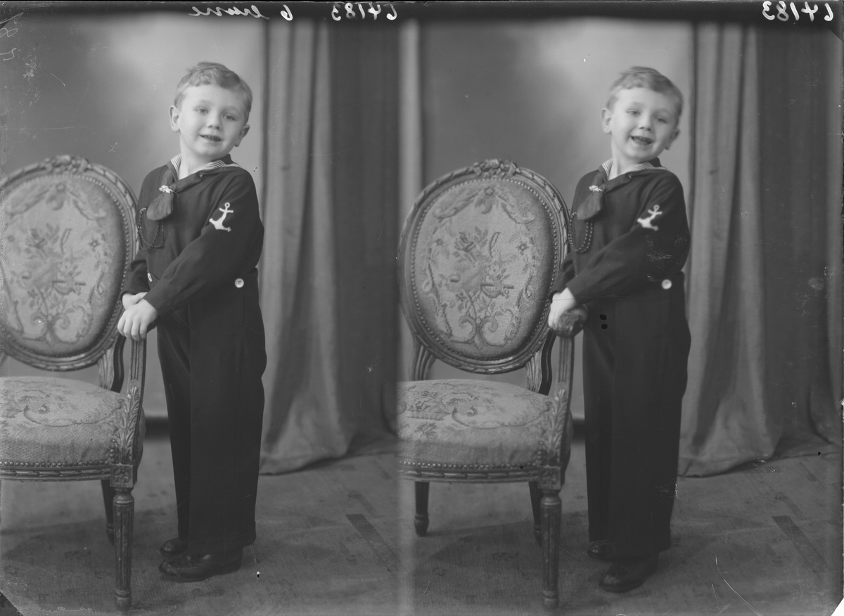 Portrett .Ung gutt med matrosdress og mørkt halstørkle poserer med hvit gyngehest og brodert stol. Bestilt av Olaf Økland. Sørhaugt. 111