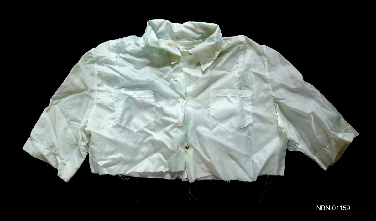 Bluse sydd av lyseblå fallskjermsilke fra andre verdenskrig. Snippkrage, 2 lommer på bringen, vertikal gjennomgående lukking over bringen med fem knapper. Trekvart lange ermer.