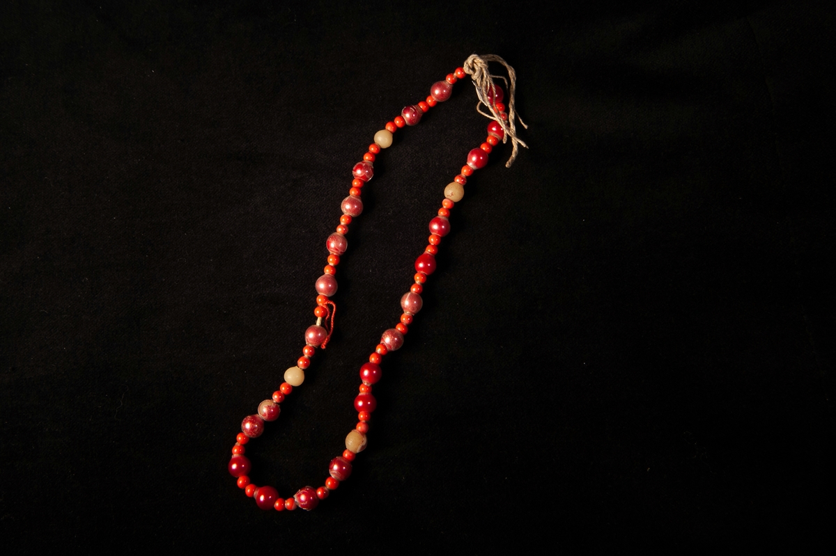 Pärlband till doppåse, JM 1776, bestående av små lackerade vaxpärlor i orangerött omväxlande med vaxpärlor lackade i rosarött, i vissa fall har lackeringen släppt.