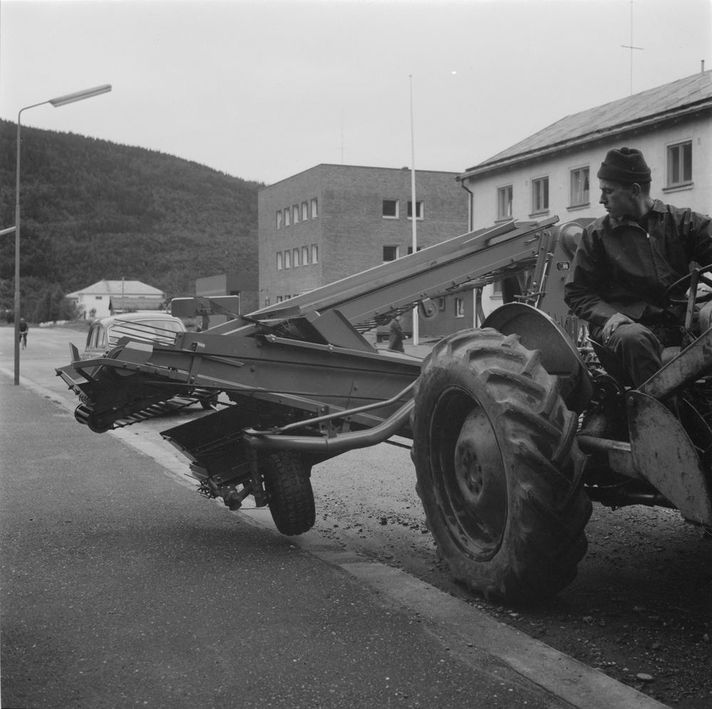 Mann med traktor med potetopptaker i Fearnleysgt. 
I bakgrunnen postkontoret og telegrafen.
Den første automatiske potetopptaker i Vefsn.