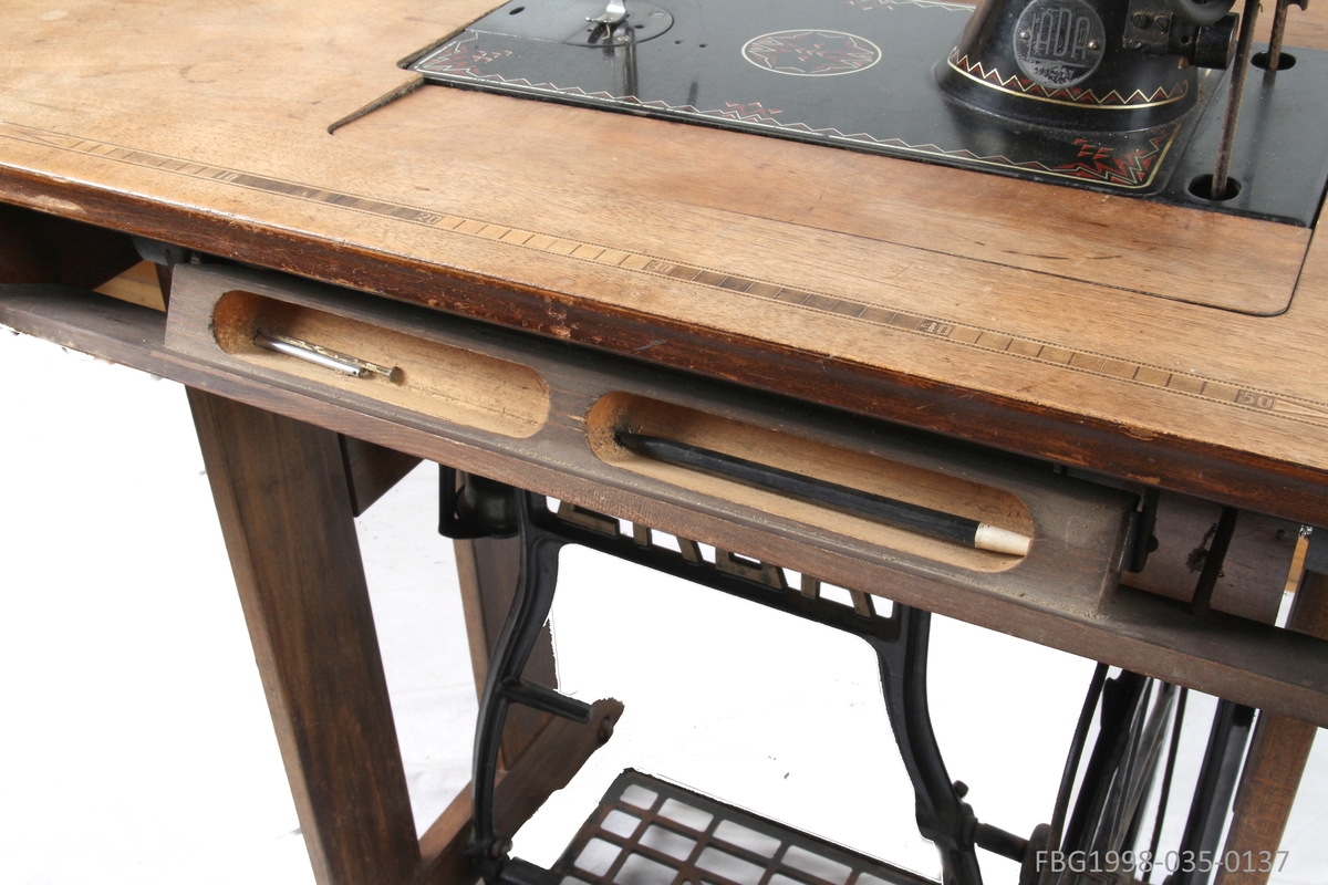 Symaskinbord med trømaskin, to låsbare skuffer til oppbevaring av sysaker. Symaskinen kan vippes ned i bordet.
