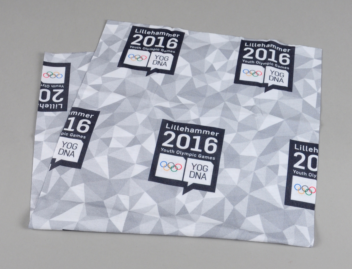 Hals av bommulsstoff som er dekorert med grått trekantmønster fra designprogrammet til Ungdoms-OL på Lillehammer 2016. Tørklet ligger i original emballasje, og det følger med oppskrift på ulike måter å bruke tørklet på.