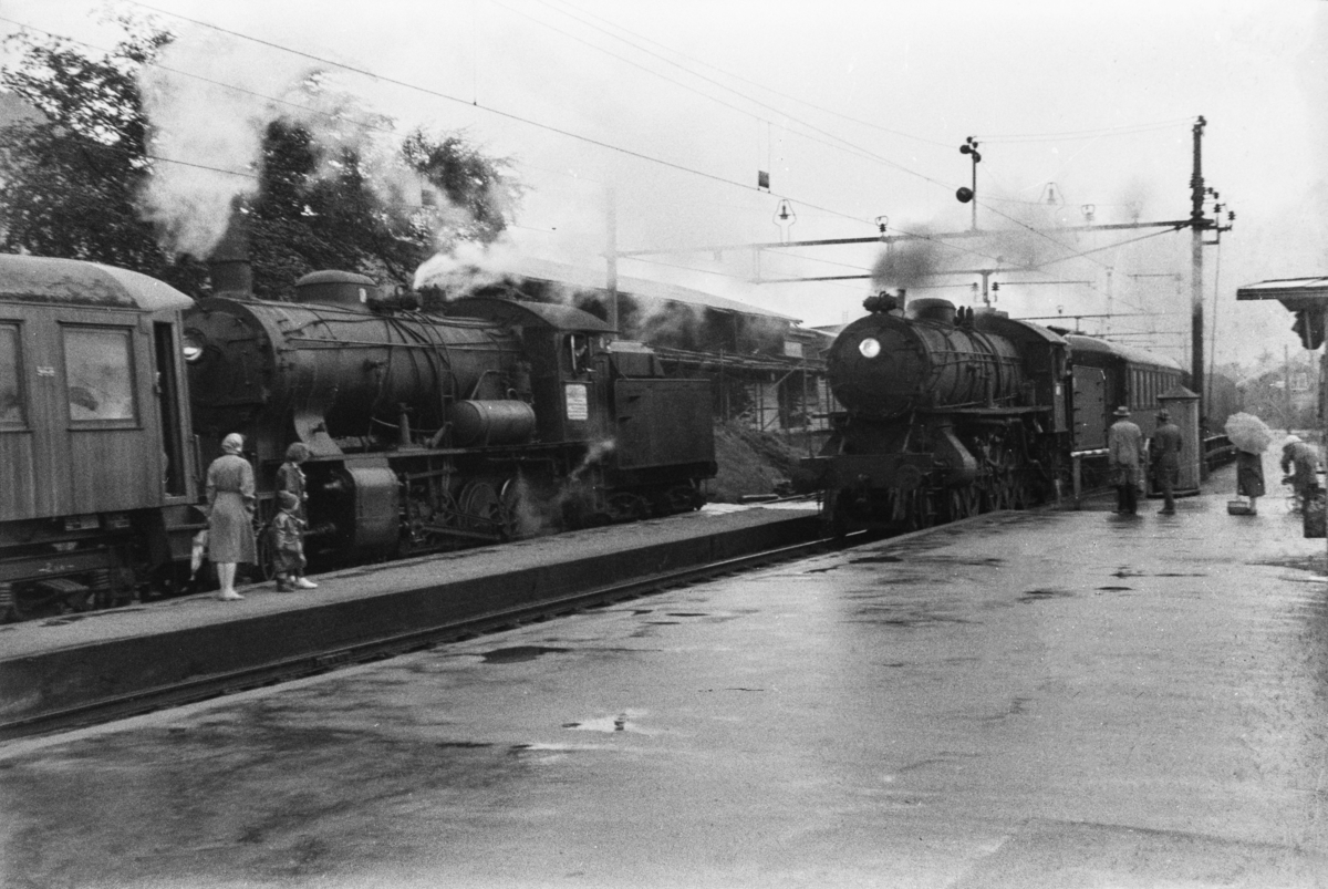 Kryssing på Minde stasjon. Til venstre damplokomotiv type 33a nr. 300 med persontog. Første vogn i toget er litra Bo4b type 3 nr. 968. Til høyre persontog med damplok type 31a nr. 319.