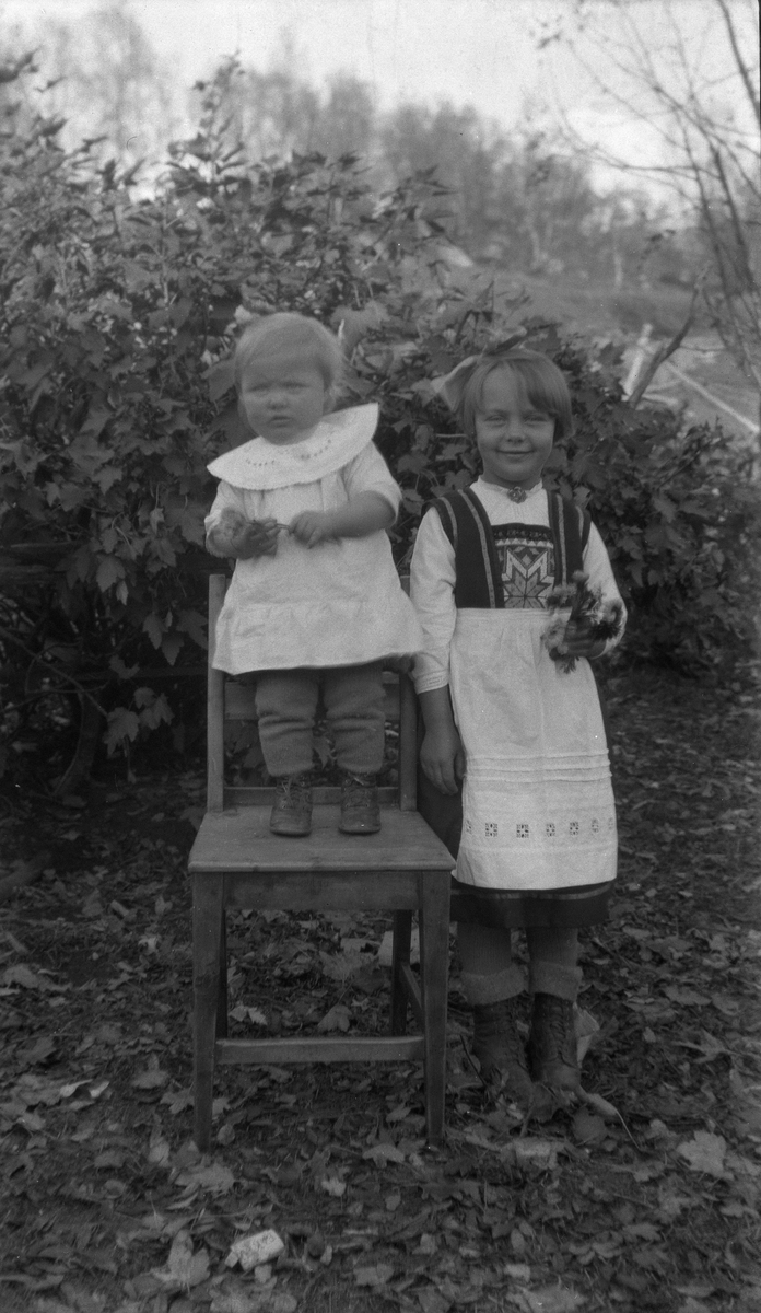 Portrett av to små piker tatt utendørs, den minste stående på en stol.