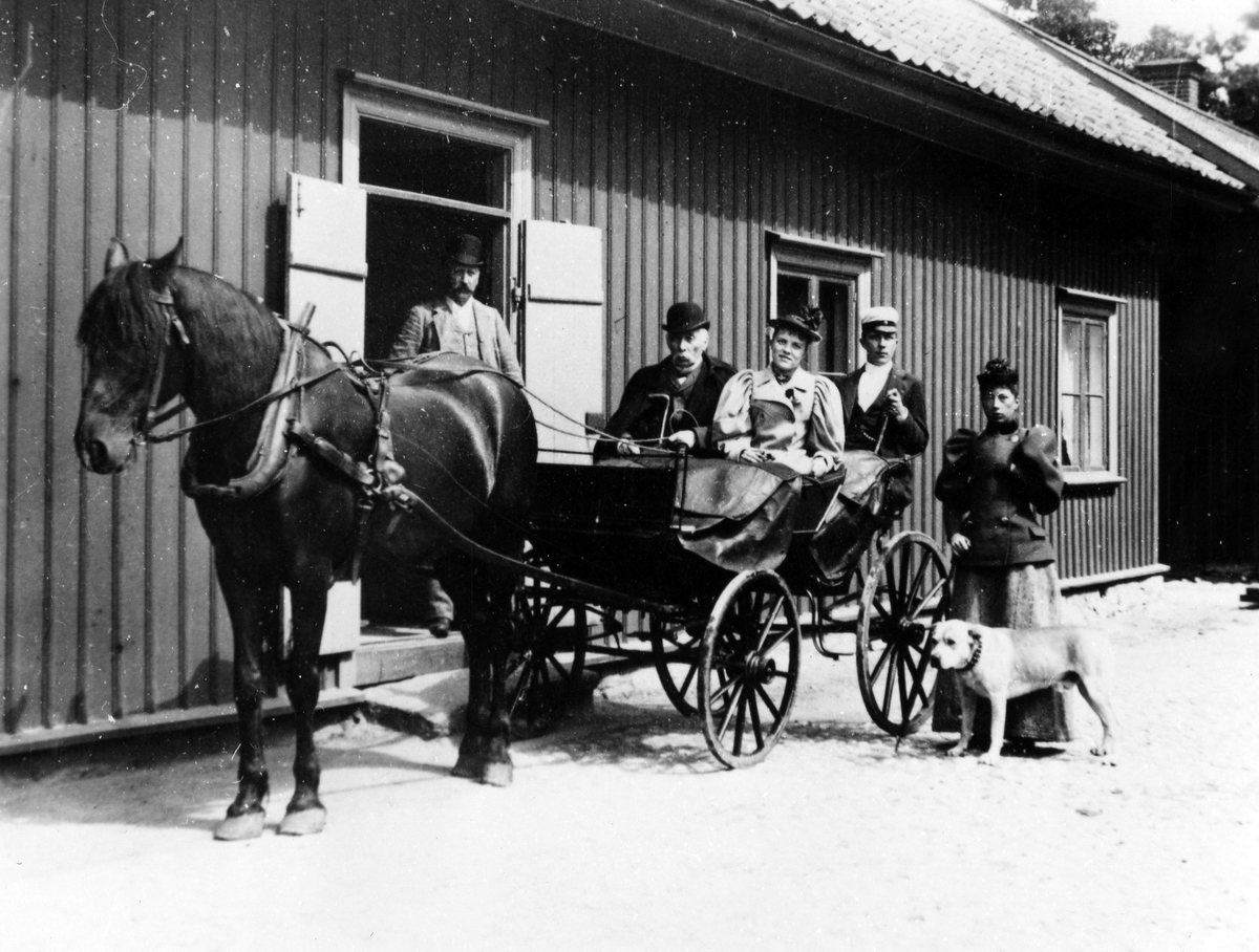 Disponent Theodor Möller, Alingsås bryggeris förste ägare, sitter tillsammans med en kvinna och en ung man i en hästdragen vagn. Vagnen står parkerad utanför en träbyggnad i vars port en man står. Bredvid vagnen står en kvinna med en hund.