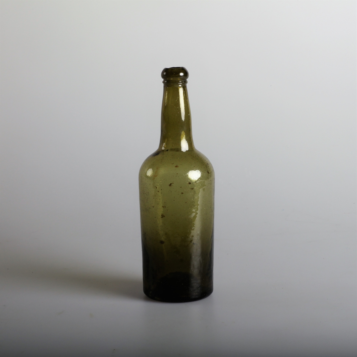 Sylindrisk flaske laget av grønt, gjennomsiktig simpel glassmasse.