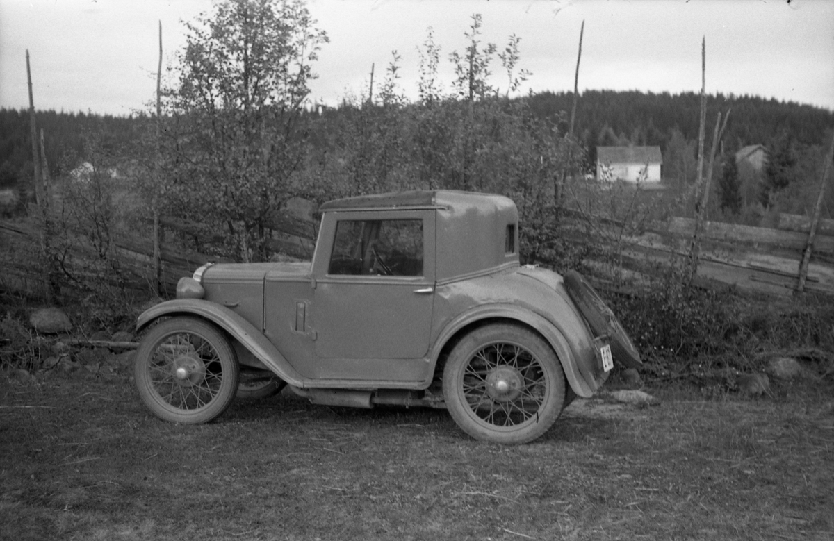 Liten bil foran et gjerde. Bilen, en Austin Seven Coupe 1928 modell, tilhørte Ole Majer. Stedet er ikke identifisert.