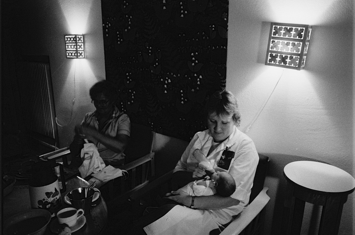 Nattpersonal på expeditionen, ett spädbarn matas med nappflaska, lättvårdsavdelningen Ringblomman, Gillbergska barnhemmet, Sysslomansgatan 37 - 39, Uppsala 1986