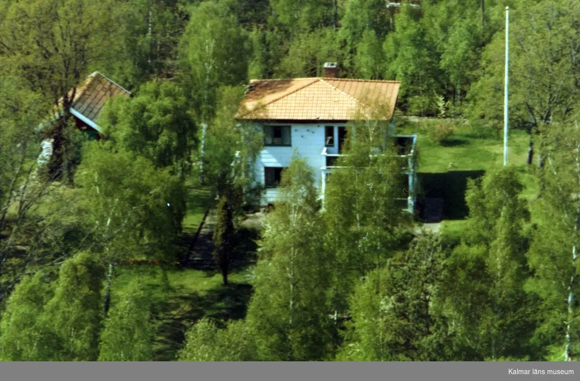 Flygfoto över Ålem. Enfamiljshus med valmat tak sidobyggnad och träd. Bild två enligt markeringen.