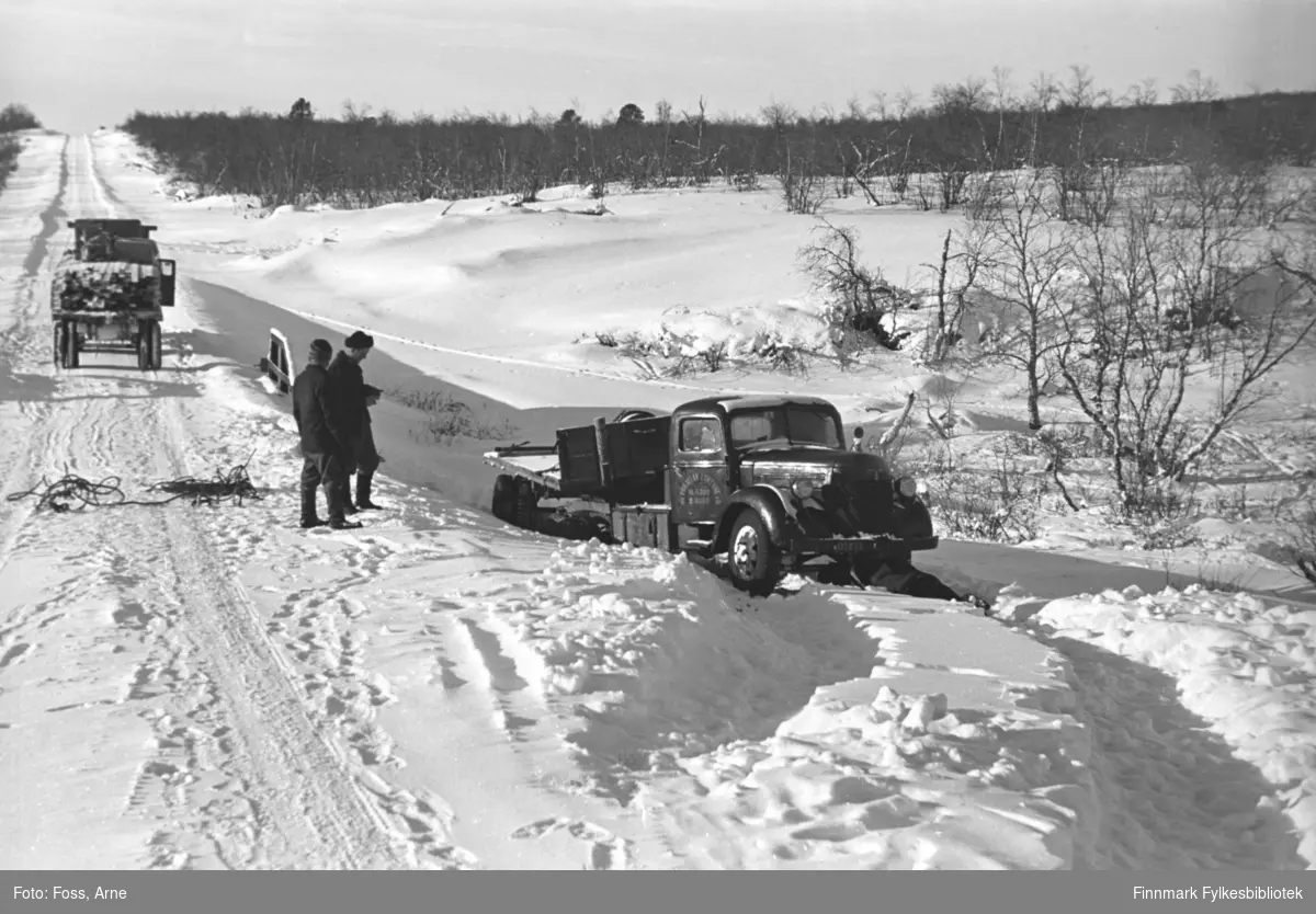 "Pohjolan Liikenne" lastebil har (antakelig?) kjørt ut av veien i Karigasniemi ved grensen til Norge (i Utsjok kommune i Finland), februar-mars 1947. En annen lastebil har stoppet i veien og er lastet med bygningsmaterialer.