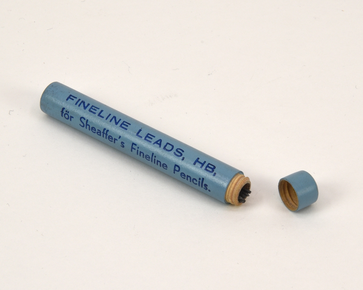 Förpackningsrör av svarvat trä med blyertsstift i HB-hårdhet. Cylindern är målad i en ljusblå nyans och har text i mörkblått: "FINELINE LEADS, HB, för Sheaffer's Fineline Pencils."