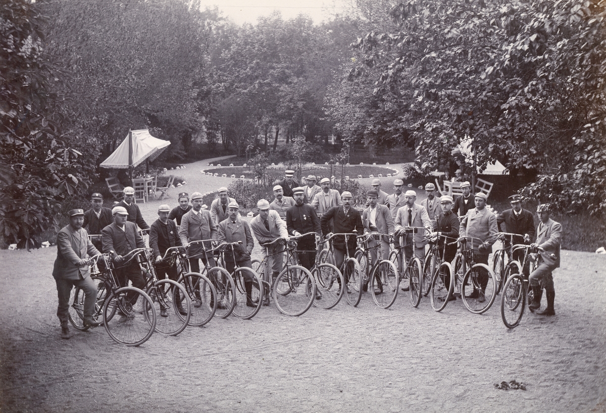 Linköpings Bicycleklubb har företagit en utfärd till Motala och här passar man på att träffa några av stadens "hjulmän" i Gästisparken. Enligt påskrift var vid tiden för bilden Wilhelm Rolén klubbens ordförande, Jean Brobeck dess vice ordförande och Gustaf Neuman föreningens sekreterare. Vi får förmoda att dessa herrar återfinns bland cyklisterna. Tiden är 1890-talets första hälft.