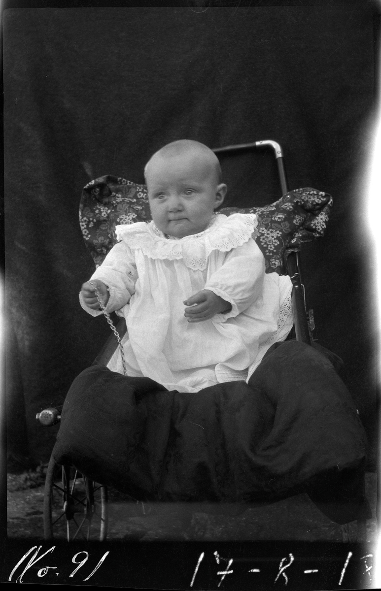Portrett av et lite barn sittende i vogn.