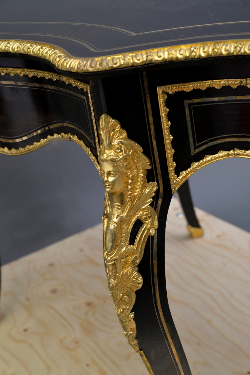 Ovalt bord (fransk), konstruksjon i heltre som er finert. Bordet har messing intarsia og pyntebeslag i metall. Overflate er antakeligvis malt med svart limfarge og lakkert.