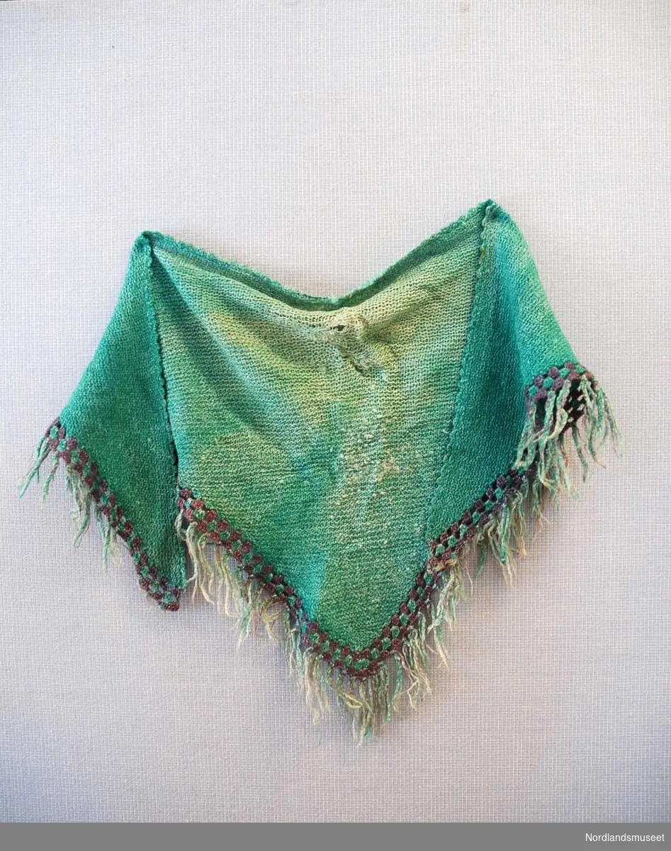 Strikket trekantformet grønt sjal med heklet lilla og grønn kant nederst. Heklet grønn bølgekant øverst. Frynser. Sjalet er slitt, og reparert flere steder.