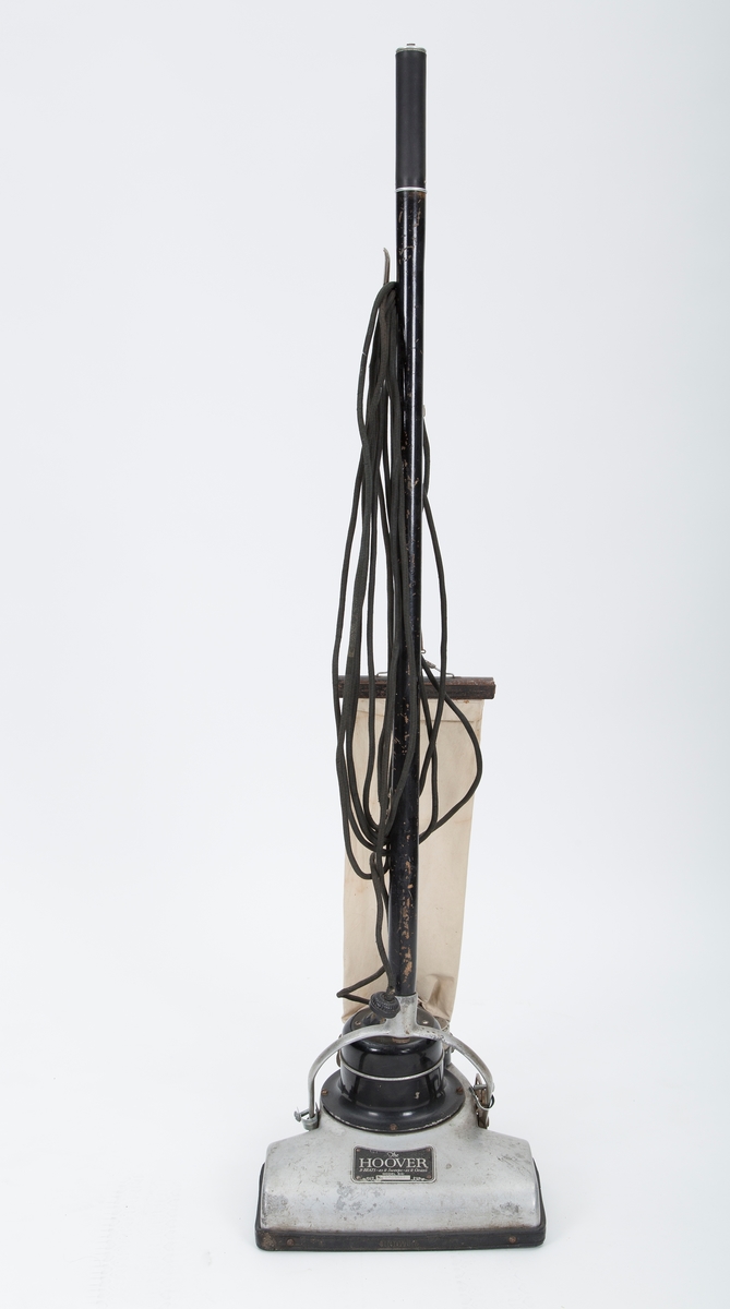 Elektrisk støvsuger. Motor og støvpose montert direkte på stang over sugemunnstykket. Stofftrukket kabel.