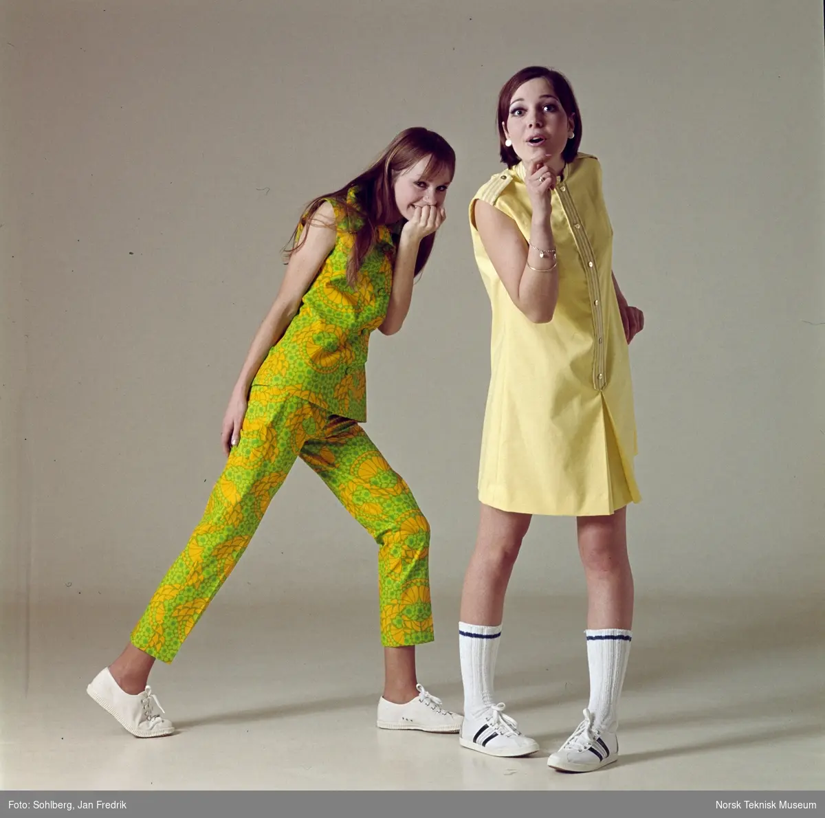 Tidlig norsk motefotografi. To unge, kvinnelige modeller viser sommermote fra 1960-tallet. Den ene har blomstermønstret bukse og topp i grønt og gult, mens den andre har kort gulmønstret kjole.