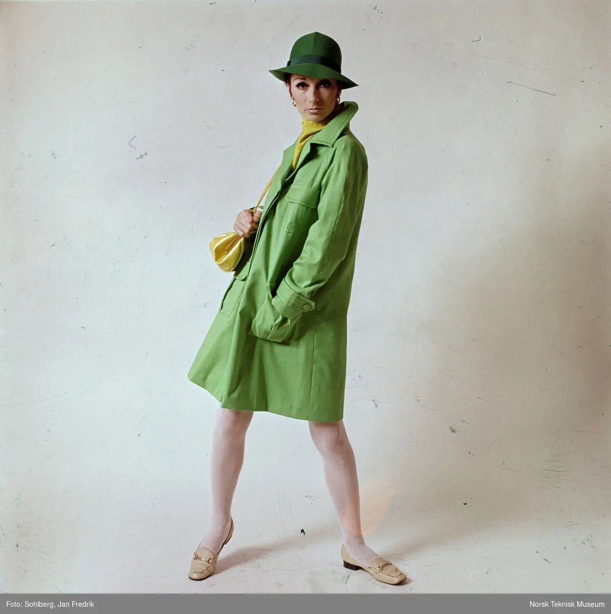 Tidlig norsk motefotografi. Kvinnelig modell med grønn kappe og hatt. Tlbehøret er en lysegrønn veske og sjerf.