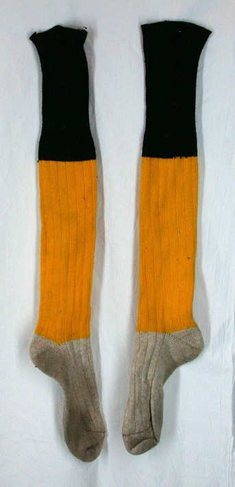 Höga resråstickade strumpor med gråvit fot och gult skaft som avslutas i svart upptill. Tryckt text i blått på sulorna som ej går att utläsa. 
Samhör med tröja (inv.nr 36619) samt shorts (inv.nr 36620).