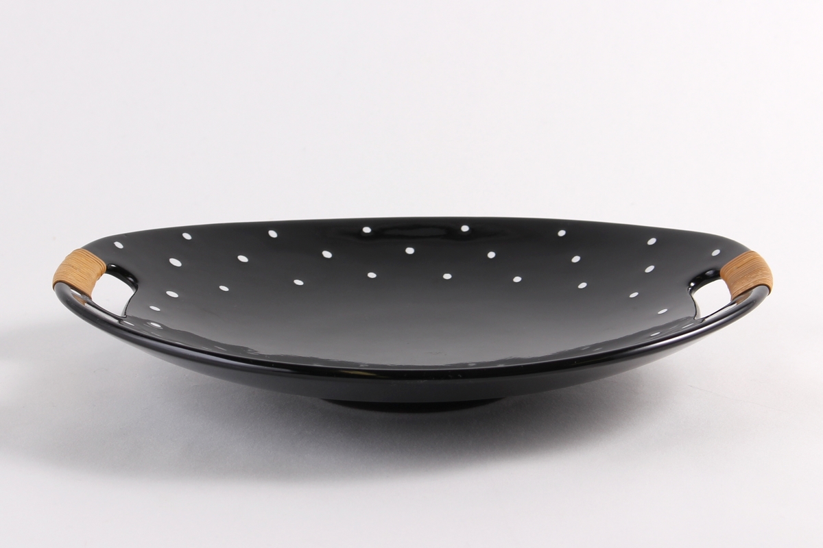 Ovalt fat med to håndtak og med blank, sort glasur dekorert med hvite prikker langs kant.