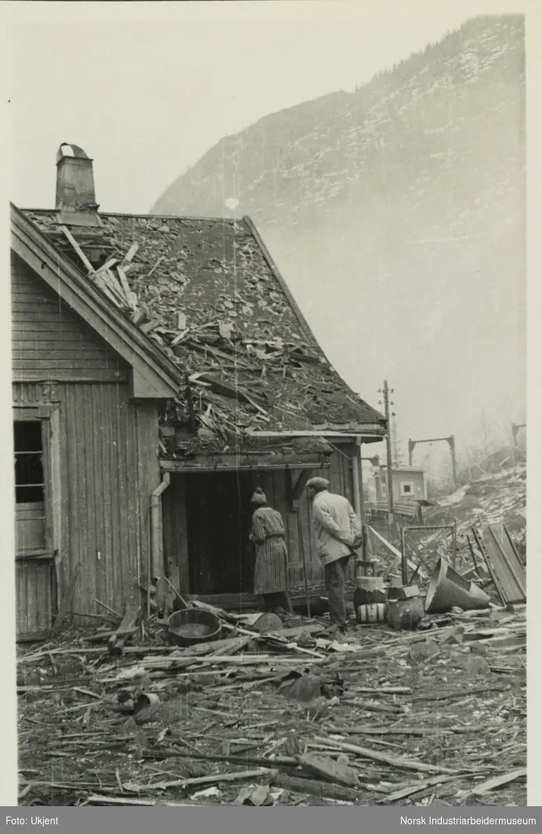 Mann og kvinne titter inn inngangsdør på ødelagt bolig etter bombinga av Vemork i 1943