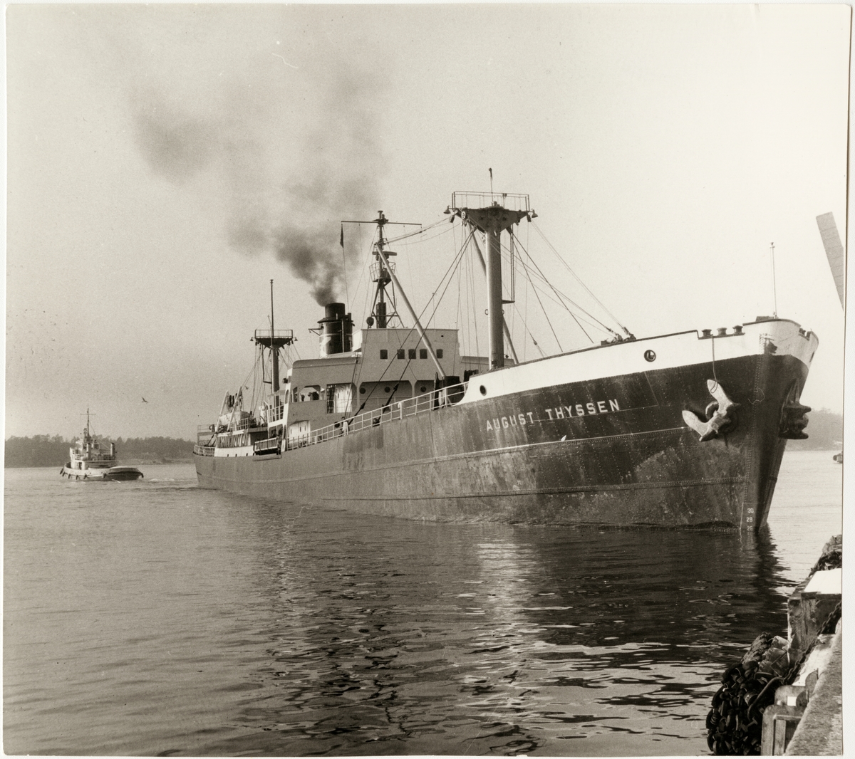 "AUGUST THYSSEN" tungt lastad med malm bogseras av "Isbjörn" från Oxelösunds hamn kaj 1964.