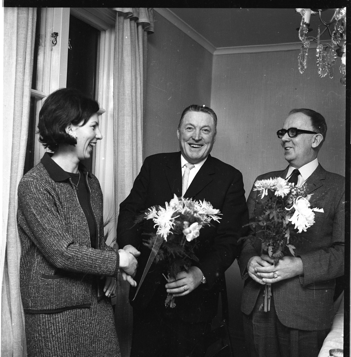 Lena von Essen skrattar och handhälsar med en glad Ture Jägenstedt som har en blomsterbukett i handen. Till höger står en lika glas Bertil Weinmer som också har en bukett.  Troligen en avtackning.