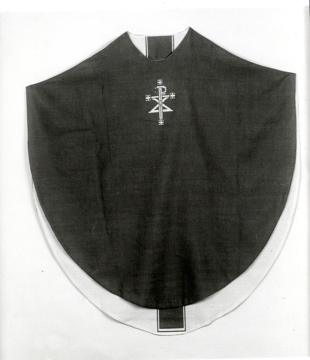 Foto (svart/vitt) av en mörk mässhake (framsidan) med broderat Kristusmonogram i ljusare färg. 

Inskrivet i huvudbok 1983.