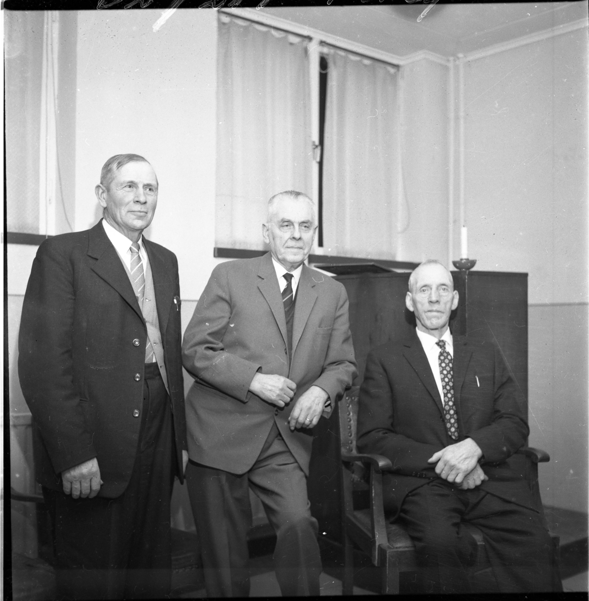 Tre män på rad i ett rum, mannen till höger sitter in en stol. De är från vänster Henning Mellin, John Ingesson och Carl Nilsson