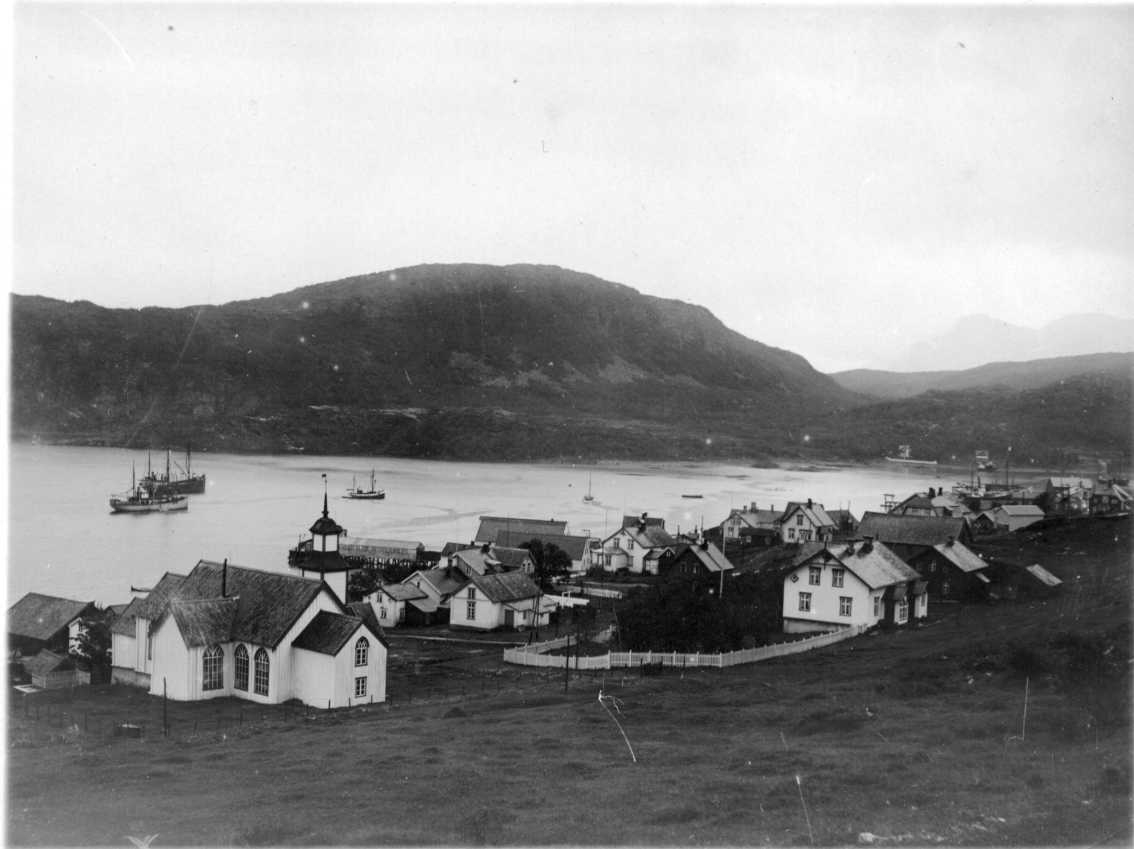 Vy över Skjaervö. Kyrkan närmast i bild till vänster. Flera båtar vid hamnen.